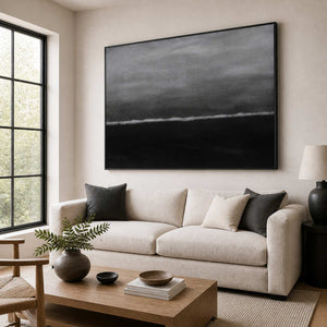 Black framed gray seascape abstraction above a cream sofa in a sunlit living room.