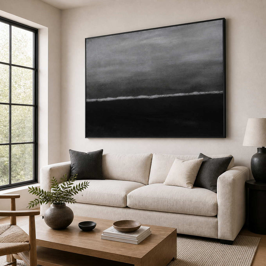 Black framed gray seascape abstraction above a cream sofa in a sunlit living room.