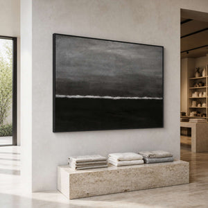 Black framed abstract wave painting above folded textiles in a natural light retail gallery.