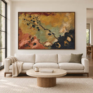 Weathered ochre, moss green and rust tones crossed by dark marks in a brown wood frame, displayed above a sofa in a living room.