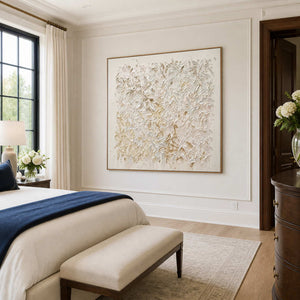Wood-framed pale textured artwork beside a cream bed with a navy throw and upholstered bench.