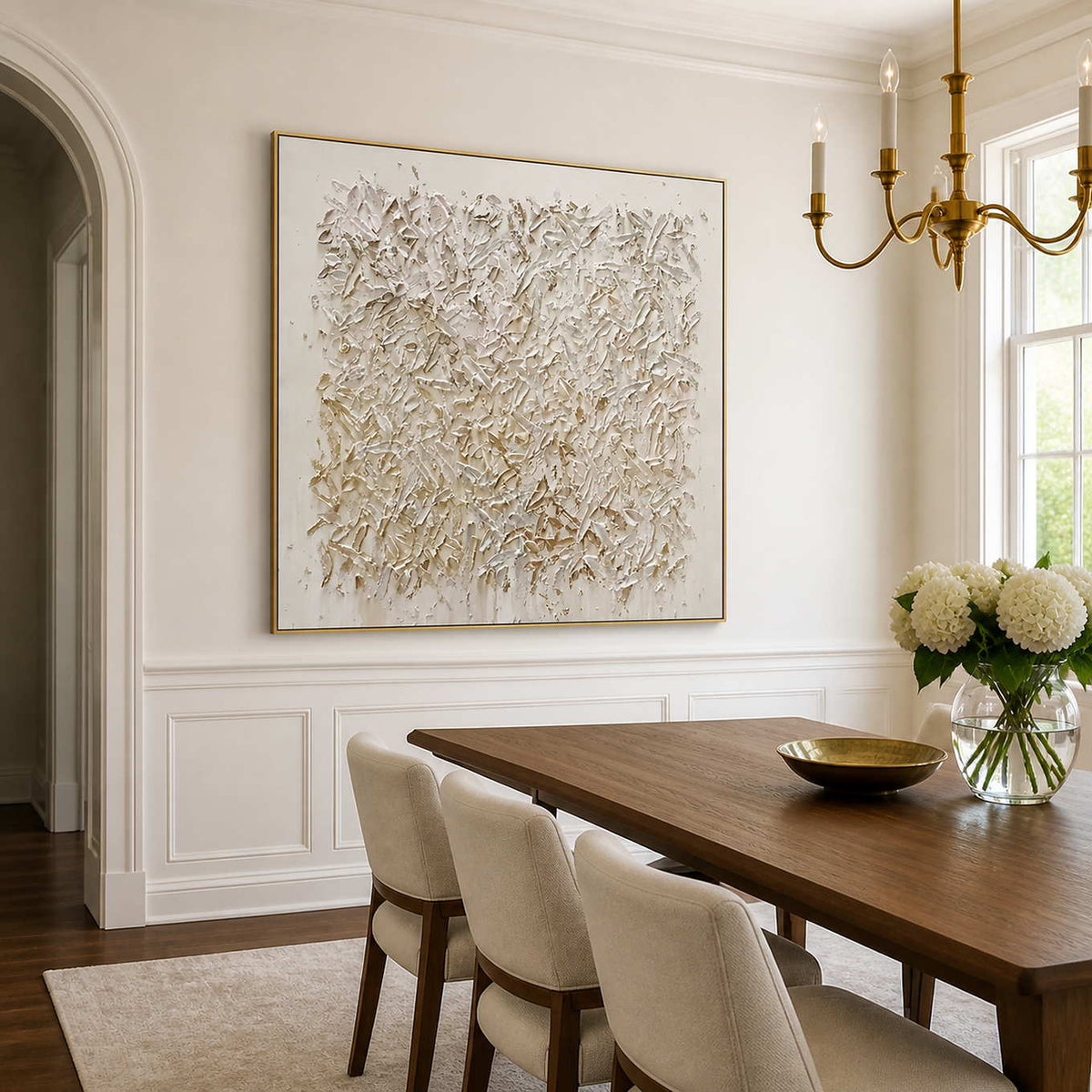 Gold-framed white textured artwork beside a wooden dining table beneath a brass chandelier.