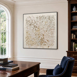 Black-framed white textured artwork beside a wooden desk and bookcase in a sunlit office.