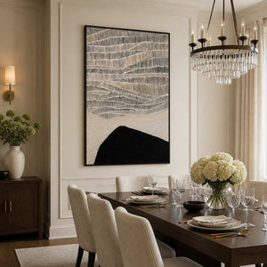Black framed textured artwork beside a dining table beneath a crystal chandelier.
