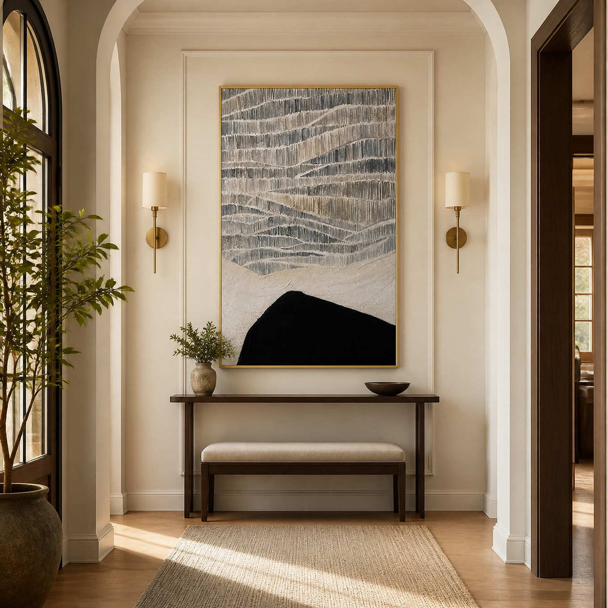 Gold framed gray and cream artwork above a narrow console in an arched hallway.