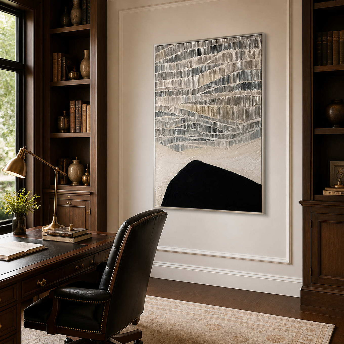 Silver framed textured abstract artwork between wooden bookshelves in a sunlit study.