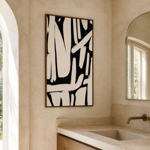 Wood framed monochrome abstract artwork above a pale stone vanity beside an arched mirror.