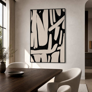 Black framed cream and black abstract artwork above a wooden dining table with pale chairs.