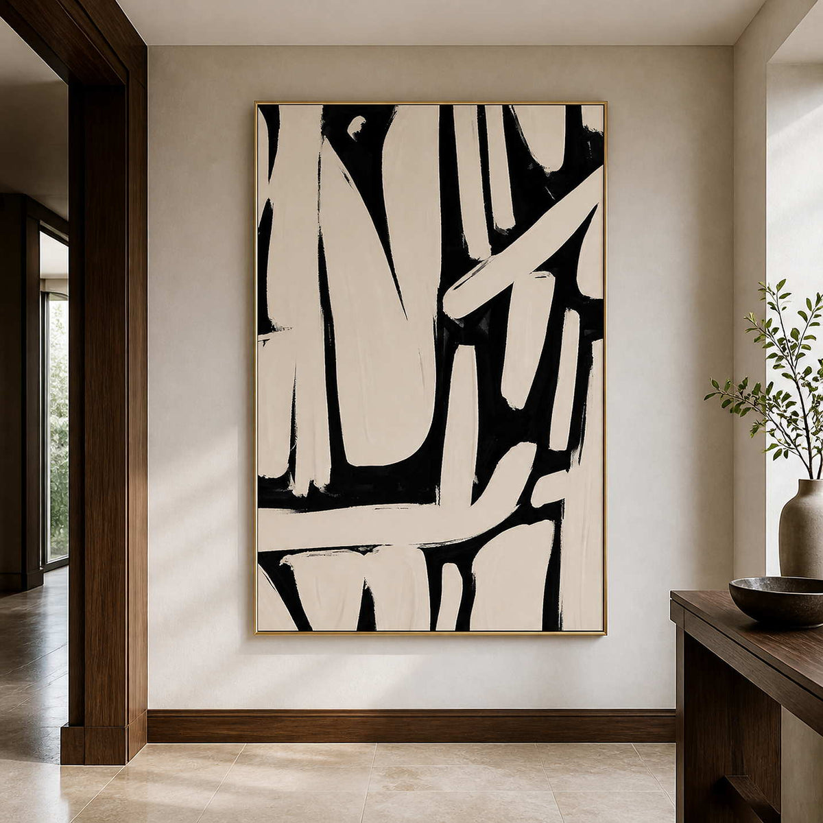 Gold framed cream and black abstract artwork beside a dark wooden console in a hallway.