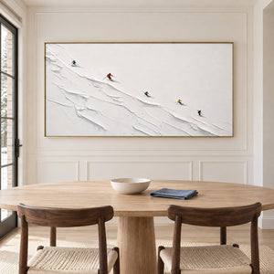 Tiny colorful skiers crossing a ridged white slope in a gold frame, displayed above a dining table.