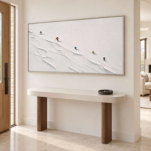 Tiny colorful skiers crossing a ridged white slope in a silver frame, displayed above an entryway console.