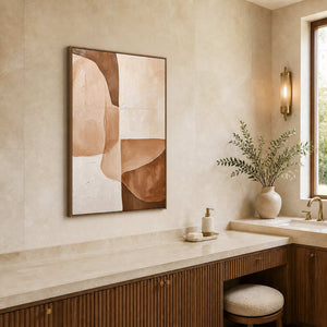 Wood-framed warm neutral abstract painting above a dressing counter beside a stone bathroom vanity.
