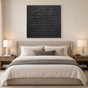 White-framed black geometric artwork above a neutral upholstered bed and paired lamps.