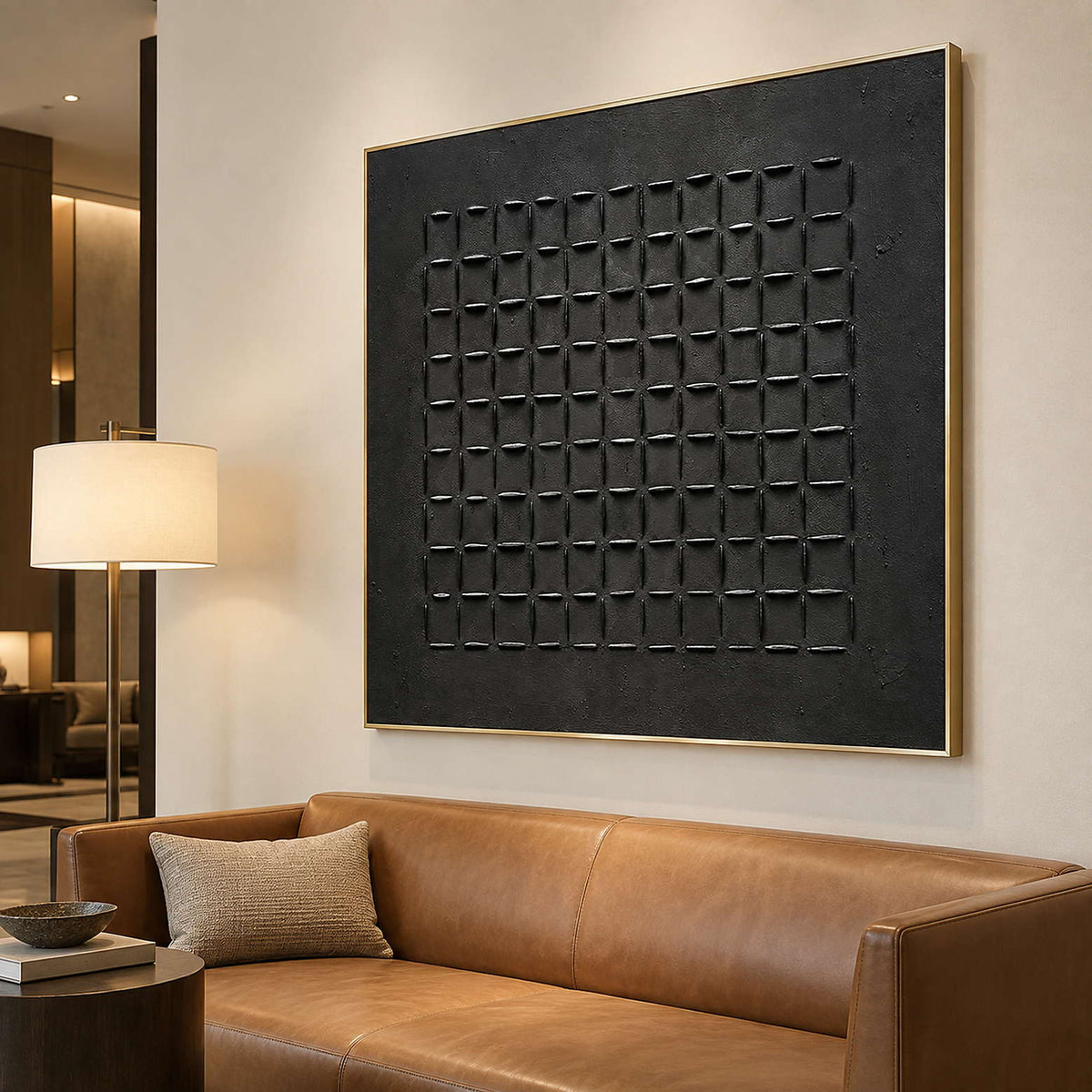 Large black geometric painting above a tan leather sofa beside a shaded floor lamp.