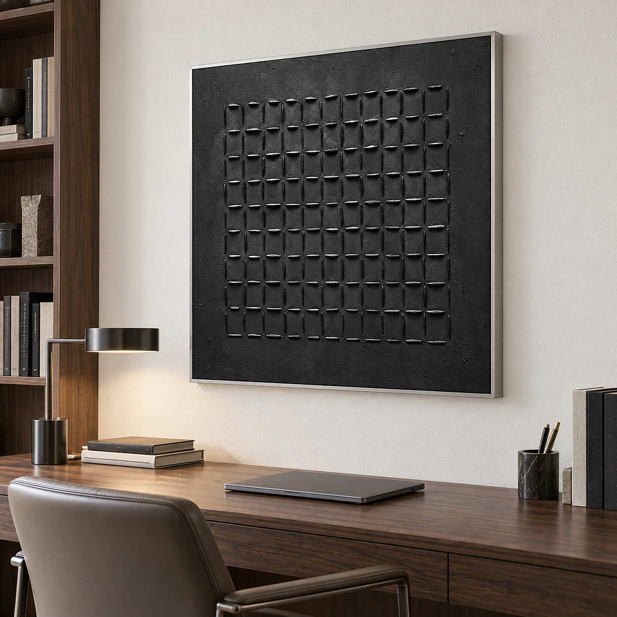 Black textured artwork above a wood desk beside bookshelves and a slim task lamp.