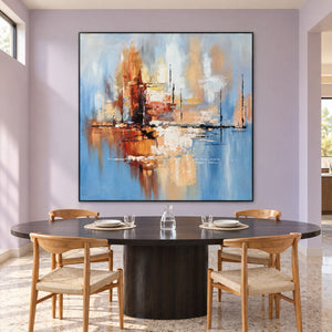 Artwork showing amber and rust blocks crossing a dark horizontal line on pale blue in a dining area beside the table, with a black frame.