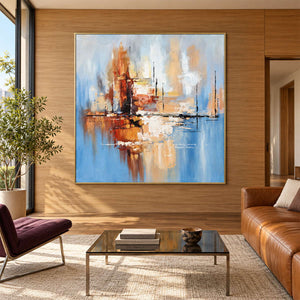 In a living room above seating, an artwork with a gold-colored frame shows amber and rust blocks crossing a dark horizontal line on pale blue.