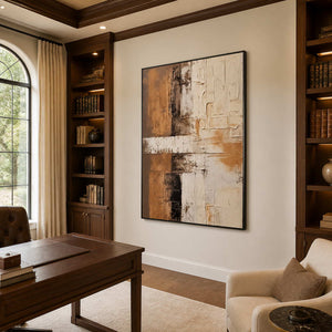 Black-framed abstract wall art between wooden bookcases in a warm study.