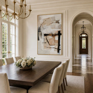 Gold framed cream and beige abstract artwork above a wooden dining table with white flowers.