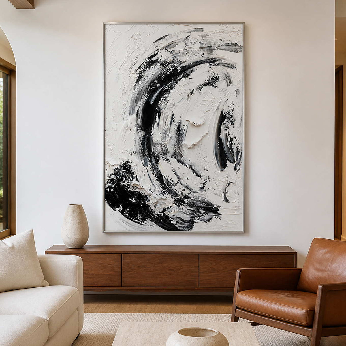 Silver framed monochrome abstract painting above a wooden cabinet beside a brown leather armchair.