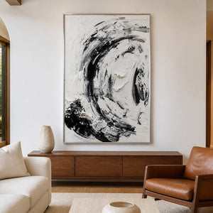 Silver framed monochrome abstract painting above a wooden cabinet beside a brown leather armchair.