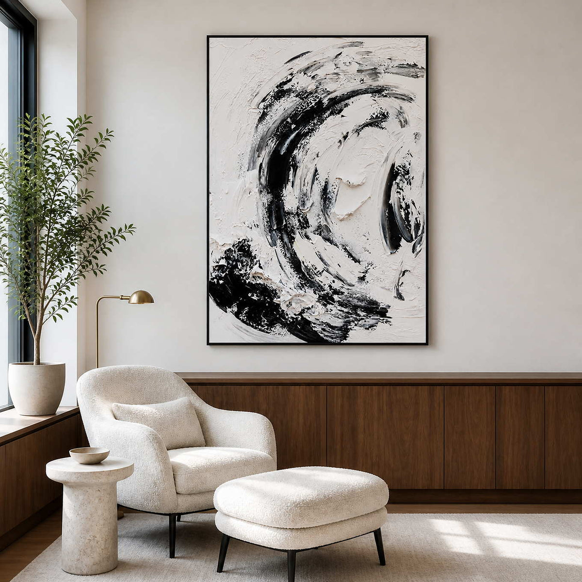 Black framed abstract painting beside a white reading chair, matching ottoman, and leafy tree.