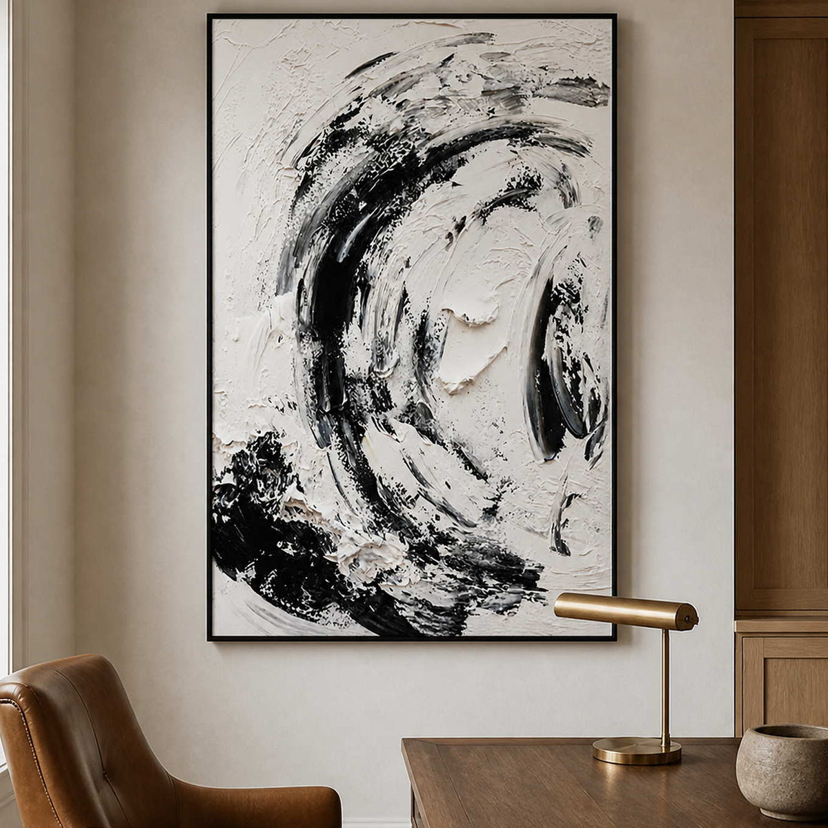 Black framed textured abstract painting beside a desk with a brass lamp and leather chair.