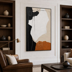 Black-framed abstract wall art between wooden bookcases in a warm home library.