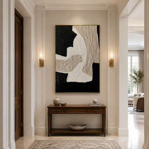 Gold framed black and white abstract painting above a slim hallway console.