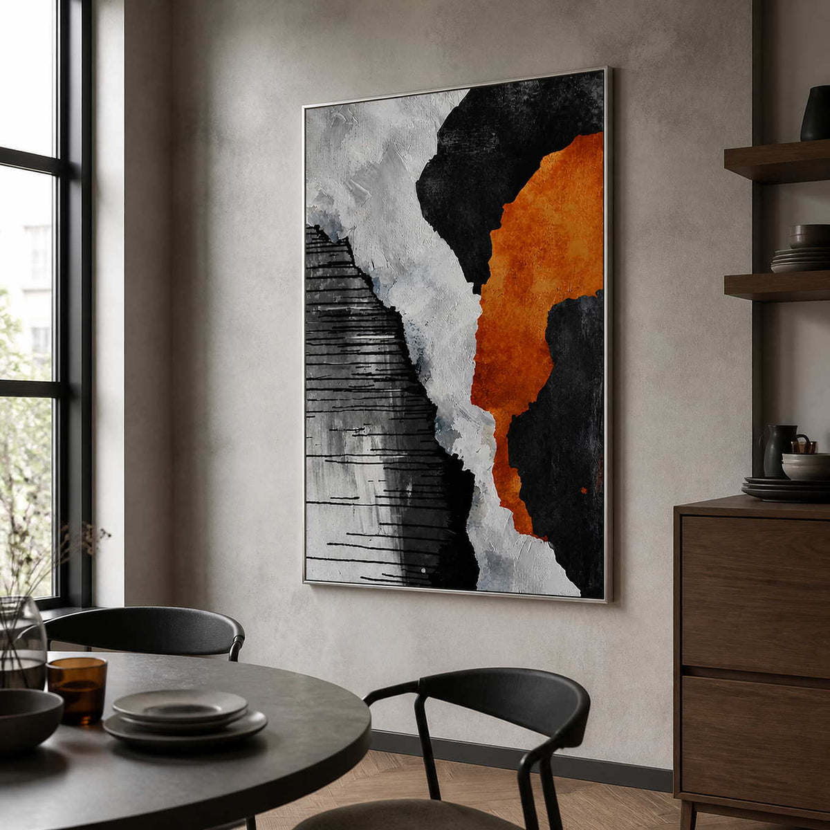 Silver framed orange and monochrome abstract artwork beside a round dark dining table and chairs.