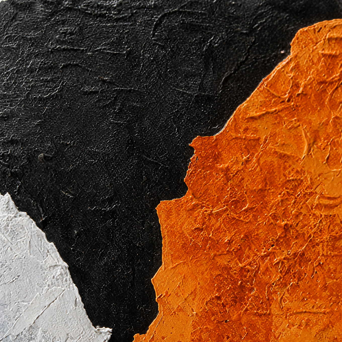 Close view of textured orange paint meeting black and white areas along uneven edges.