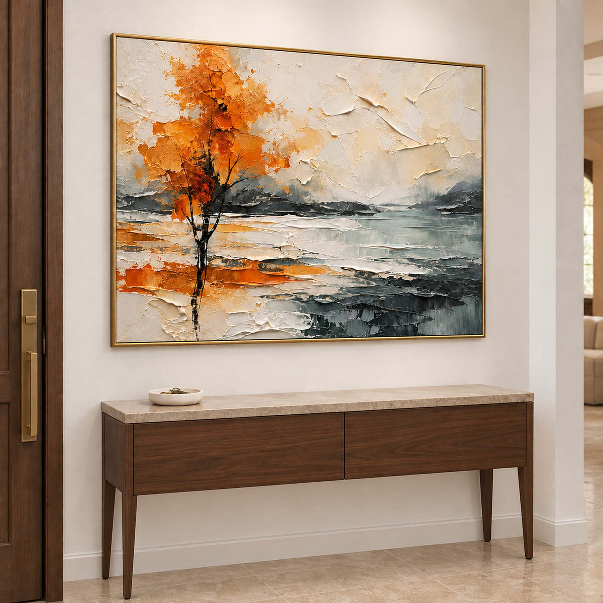 An orange autumn tree reflected beside a gray lake in a gold frame, displayed above an entryway console.