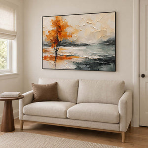 An orange autumn tree reflected beside a gray lake in a black frame, displayed beside seating in a lounge.