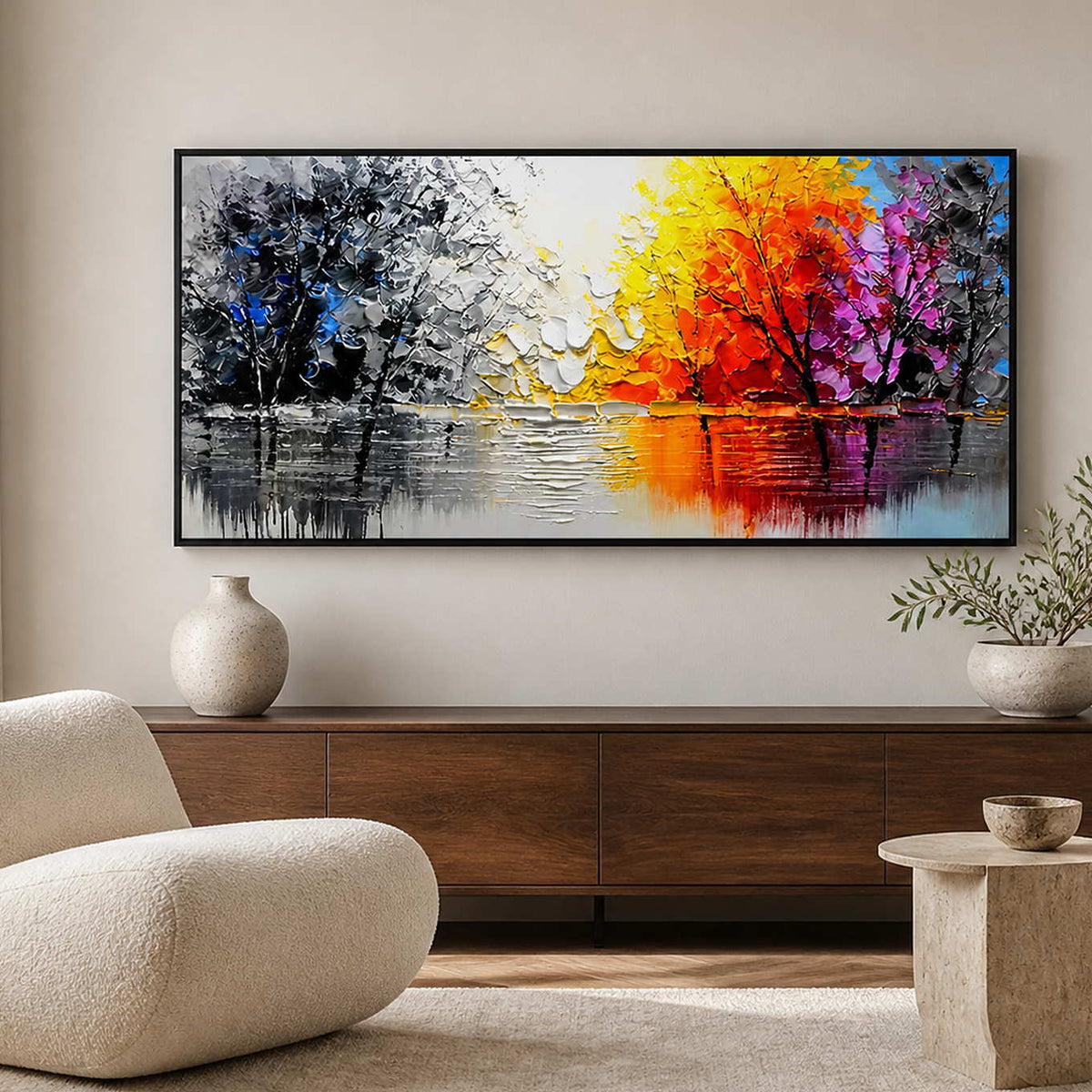 Black-framed autumn lake painting above a low cabinet beside a rounded reading chair.