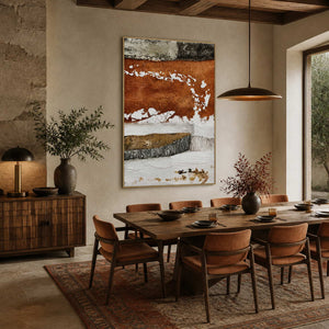 Gold framed rust and white abstract artwork overlooking a wooden dining table and upholstered chairs.