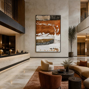Black framed rust and white artwork beside a hotel reception desk in a tall lobby.