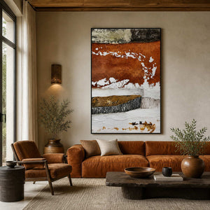 Black framed rust and white abstract artwork above a warm leather sofa beside tall windows.
