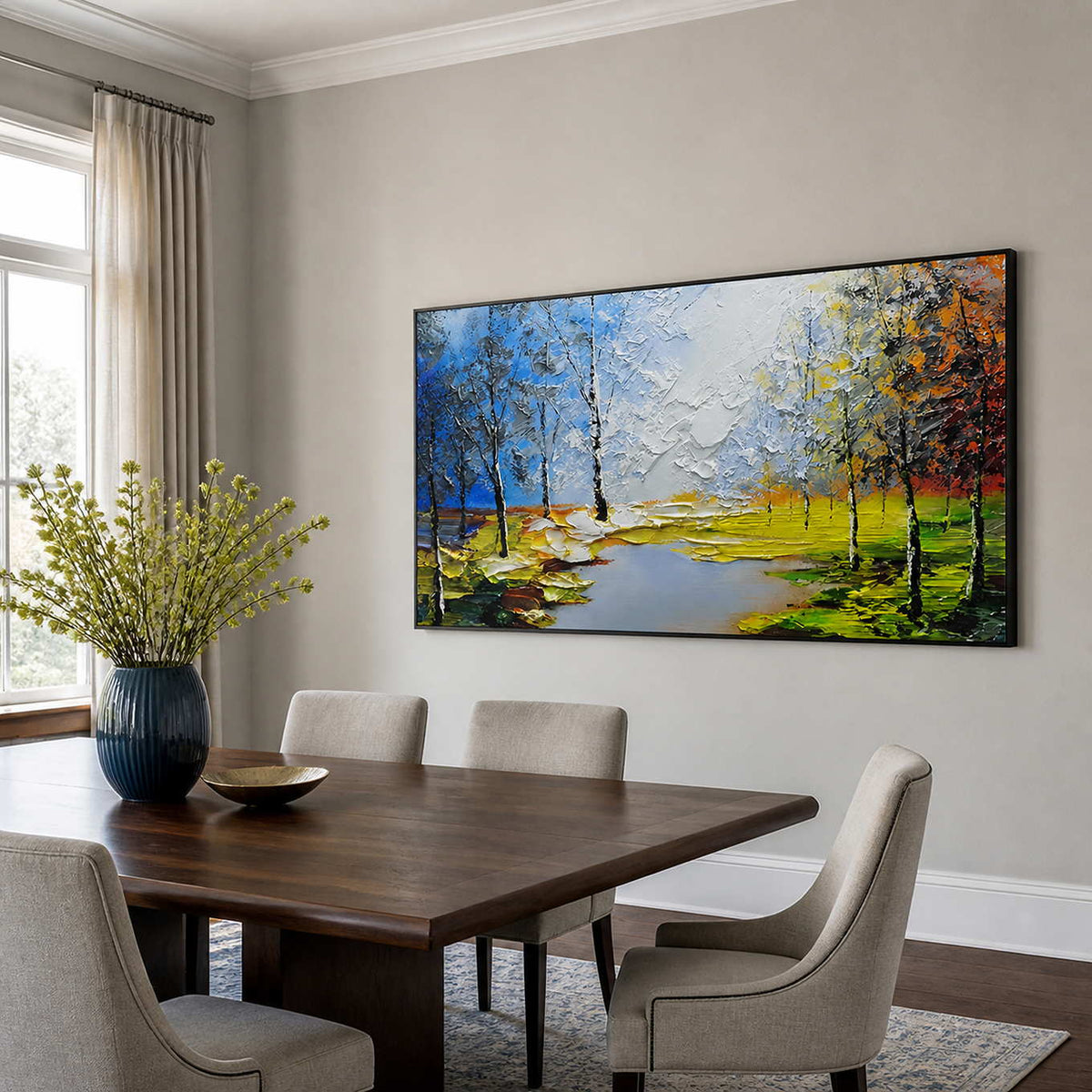 Black framed autumn landscape painting with slender trees beside a wooden dining table.