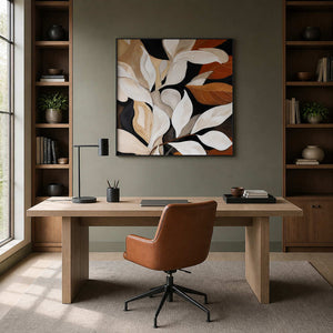 Black framed square leaf painting between bookshelves behind a home study desk.