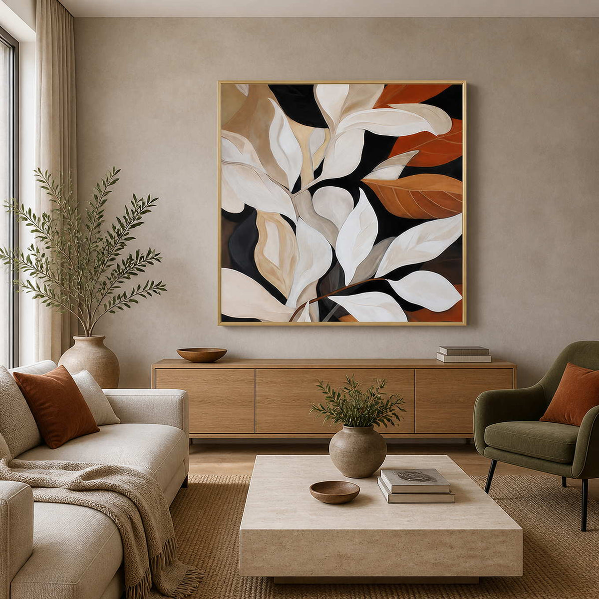 Gold framed botanical painting with cream and rust leaves in a bright living room.