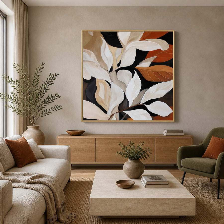 Gold framed botanical painting with cream and rust leaves in a bright living room.