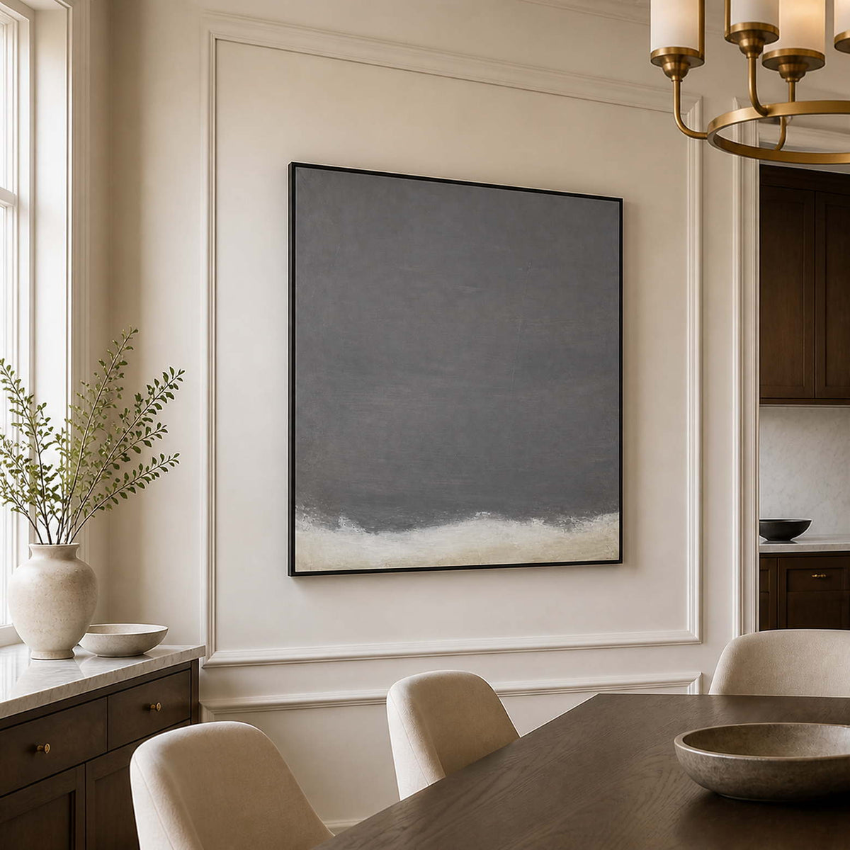 Black framed tonal abstract painting beside a dining table in a cream paneled room.