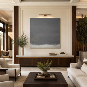 Gold framed square abstract painting with a pale lower edge above a hotel lobby console.