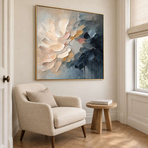 Layered cream and blush petals fading into deep blue in a gold frame, displayed beside seating in a lounge.