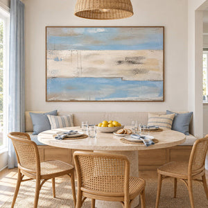 Pale blue and ivory coastal abstract painting with sand and charcoal bands in a brown wood frame in a dining room.
