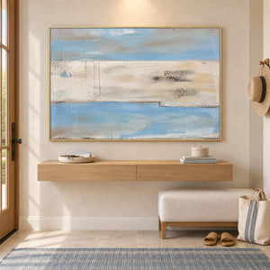 Pale blue and ivory coastal abstract painting with sand and charcoal bands in a gold frame in an entryway.