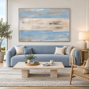 Pale blue and ivory coastal abstract painting with sand and charcoal bands in a silver frame in a living room.