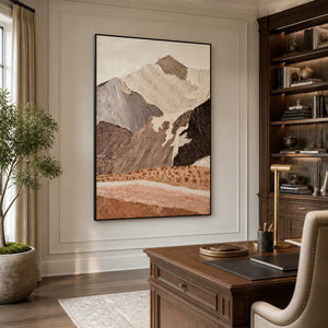 Black framed textured mountain artwork beside wooden bookshelves and a desk in a home office.