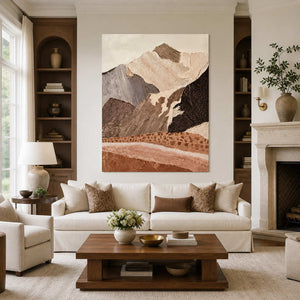 Frameless textured mountain artwork above a cream sofa between wooden shelves and a stone fireplace.