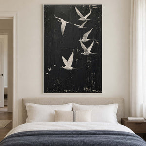 White birds flying across a charcoal-black sky in a white frame, displayed above a bed.